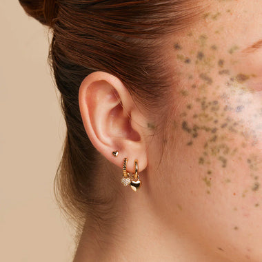 Side profile of a woman wearing matching Astrid & Miyu crystal huggies and ear cuffs in gold.